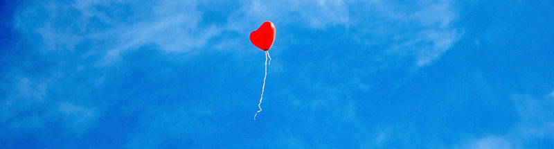 Roter Luftballon in Herzform steigt in einen blauen Himmel auf